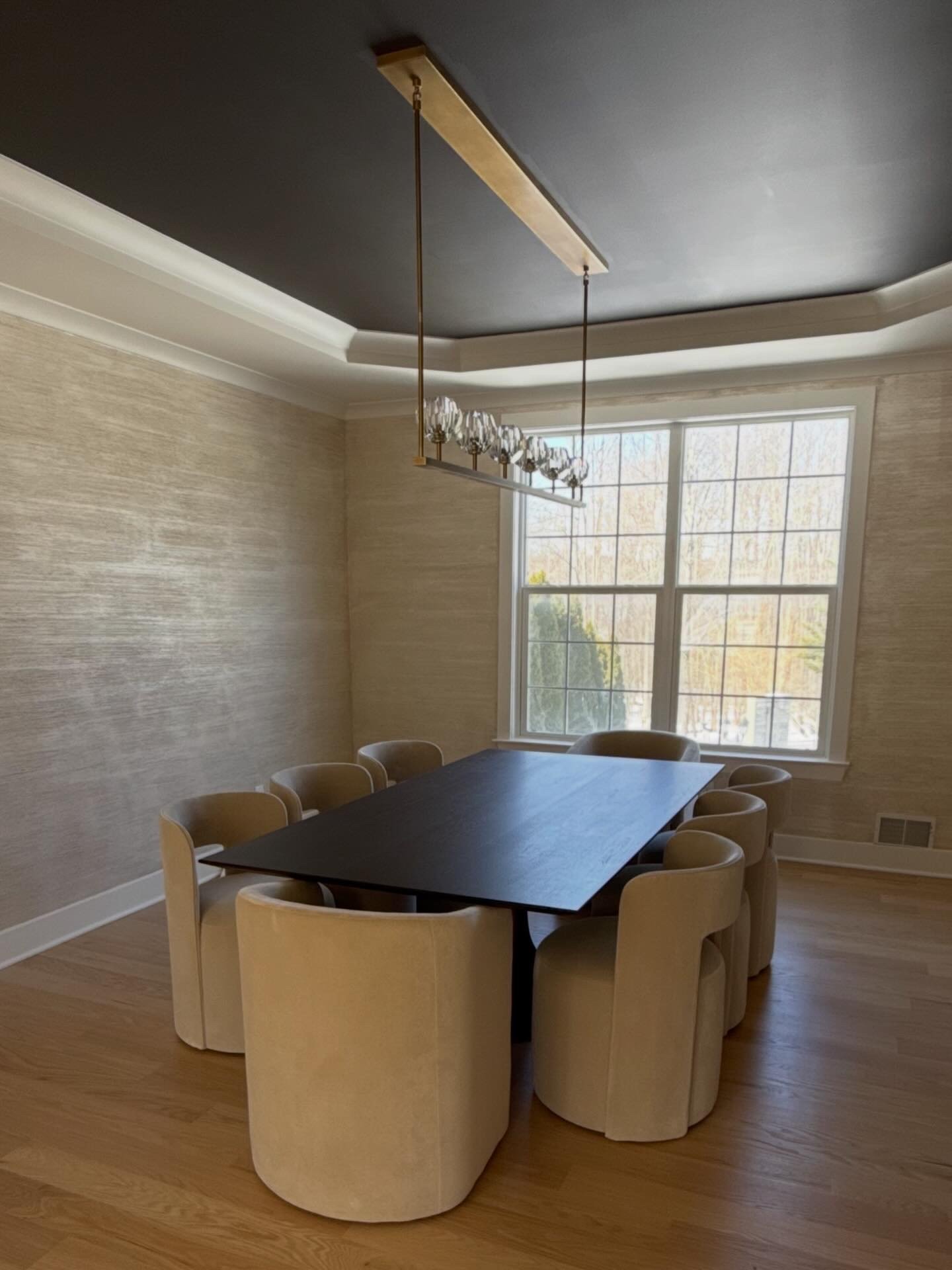 Dining room with dark lacquered tray ceiling, grasscloth walls, black table, and sculptural barrel chairs