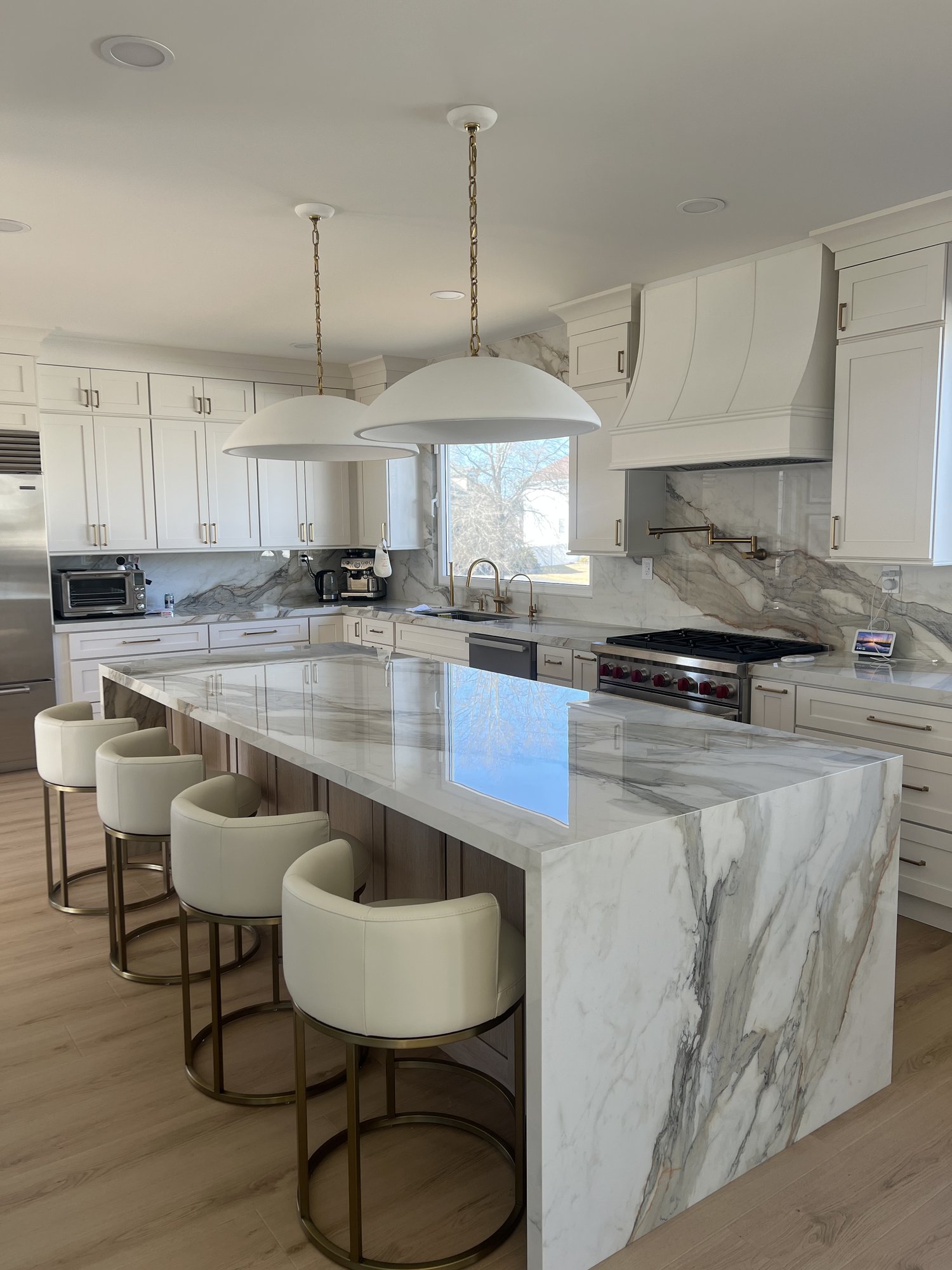 Kitchen with white cabinetry, dome pendants, marble waterfall island, and brass bar stools