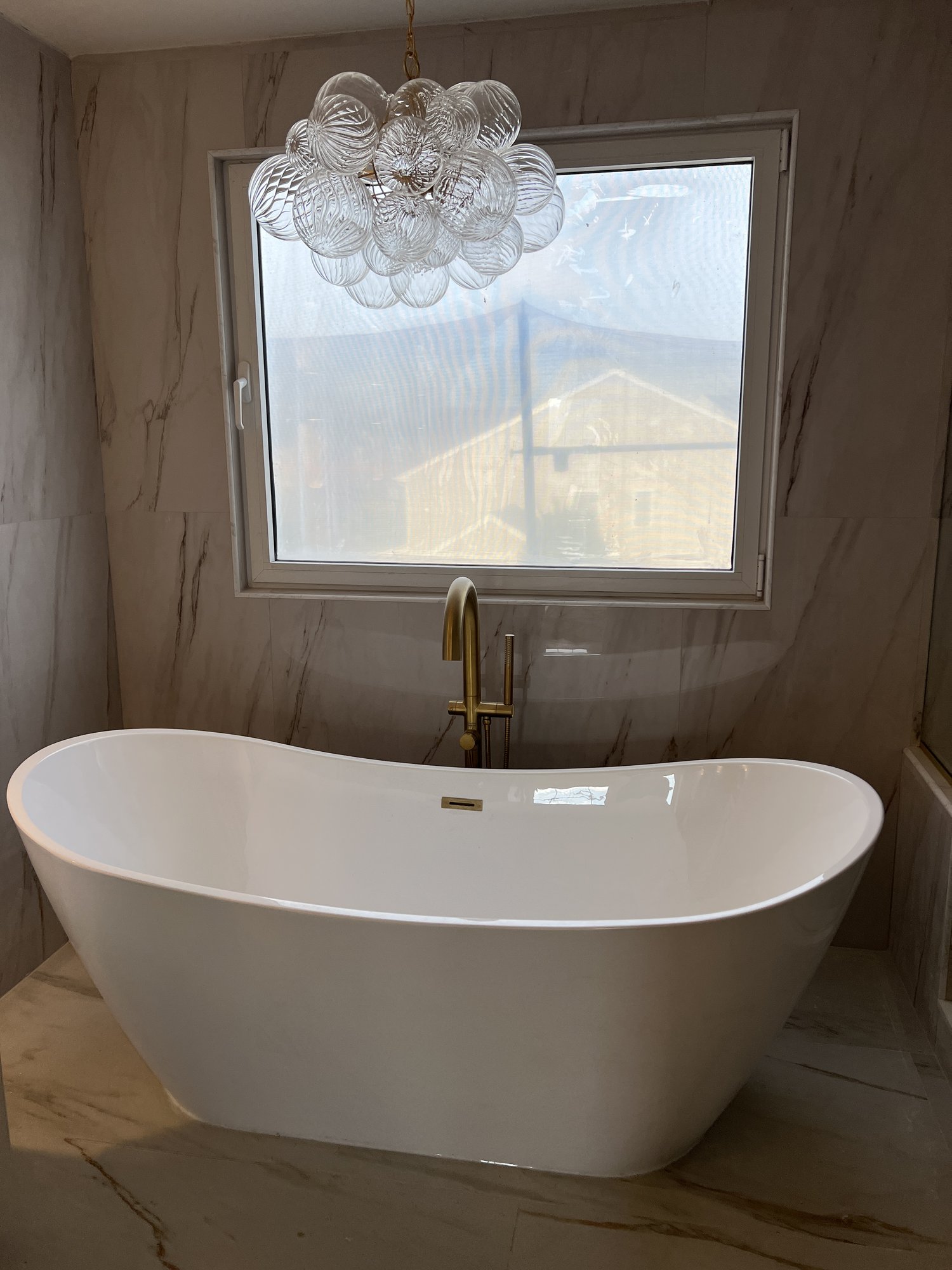 Primary bathroom with freestanding soaking tub, marble walls, and bubble chandelier