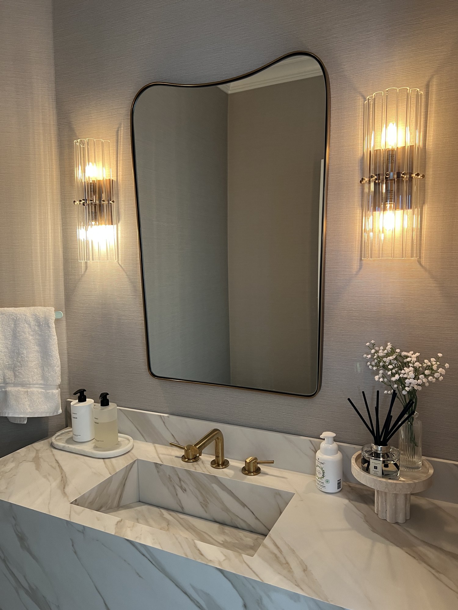 Powder room with curved mirror, crystal sconces, and marble vanity