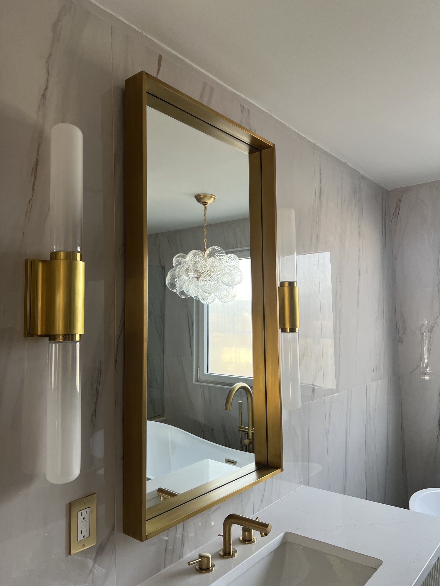 Bathroom vanity with gold-framed mirror and brass tube sconces
